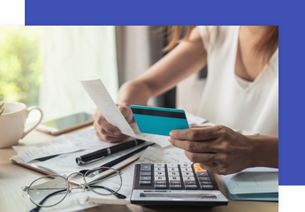 person sitting at a desk holding a credit card and a bill to pay